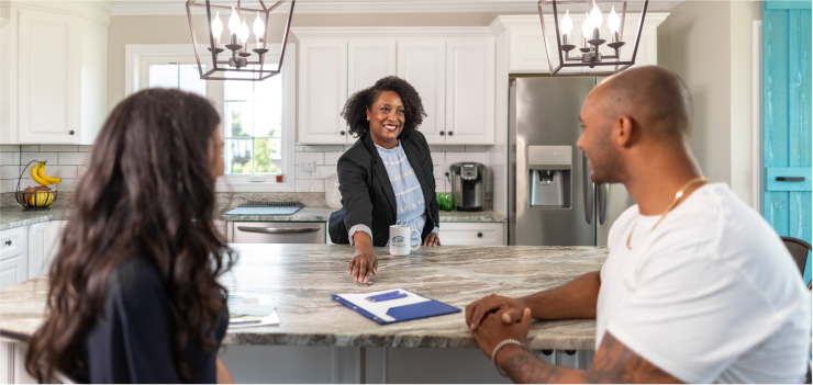 Female real estate agent handing over information to a man and woman in their kitchen