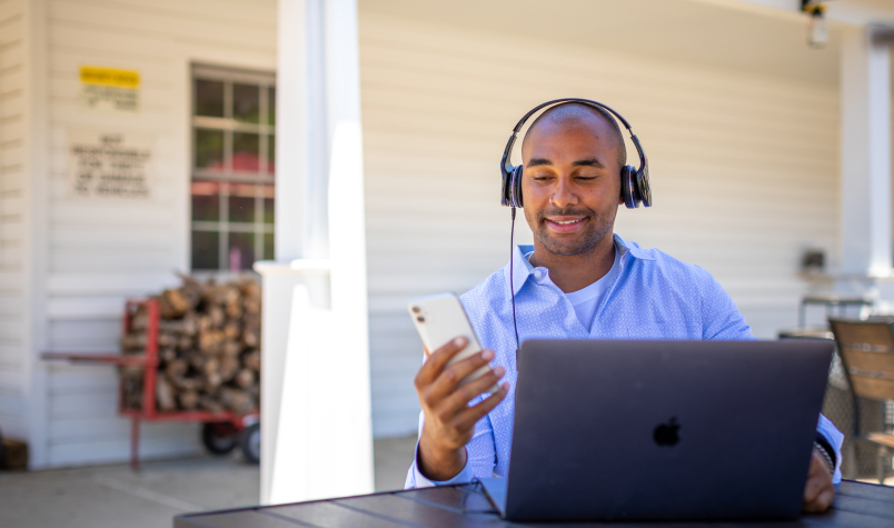 Man with Headphones Using a Phone and Laptop