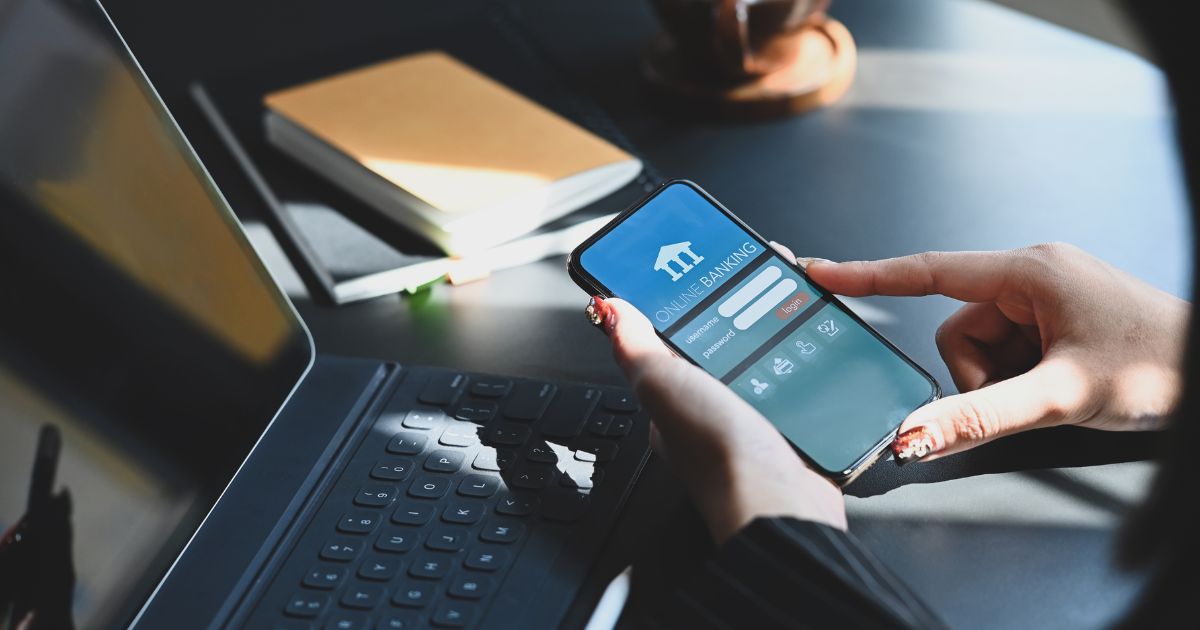 Person using online banking app on mobile phone next to tablet