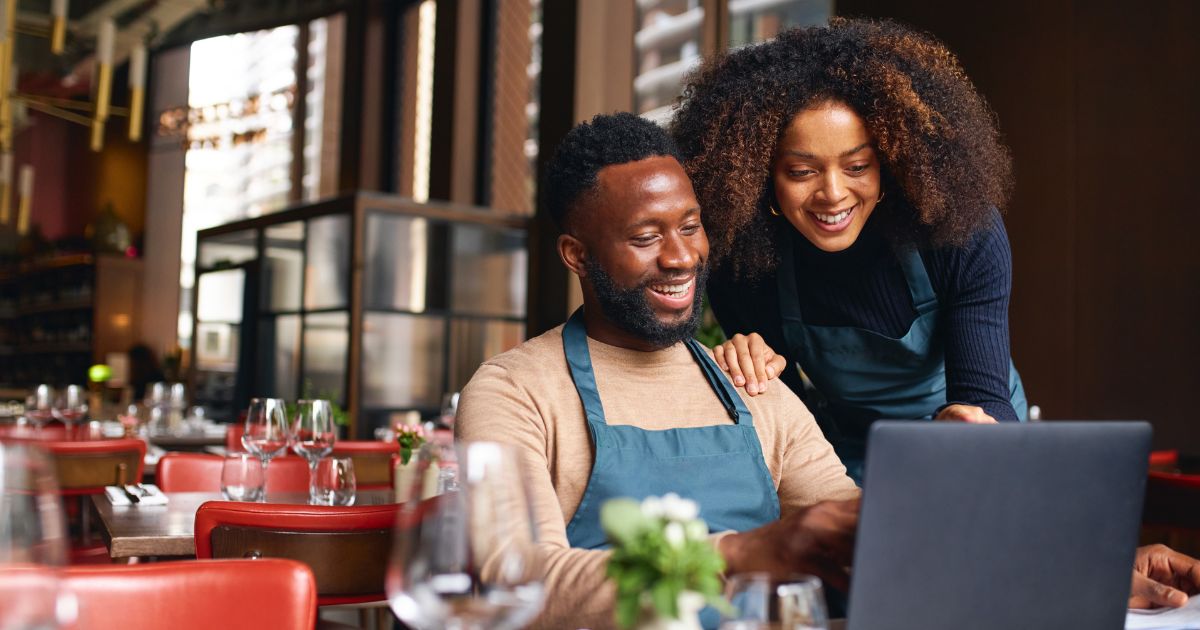 Man and woman restaurant owners using laptop in restaurant setting.