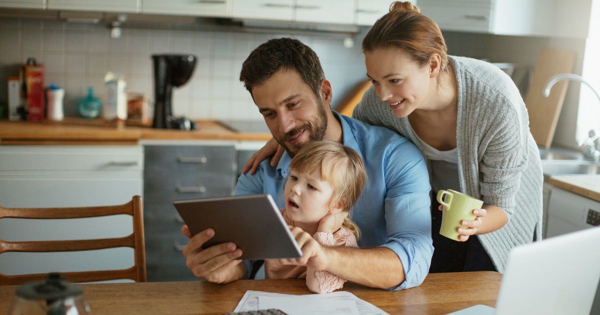 Couple with toddler reading a tablet.