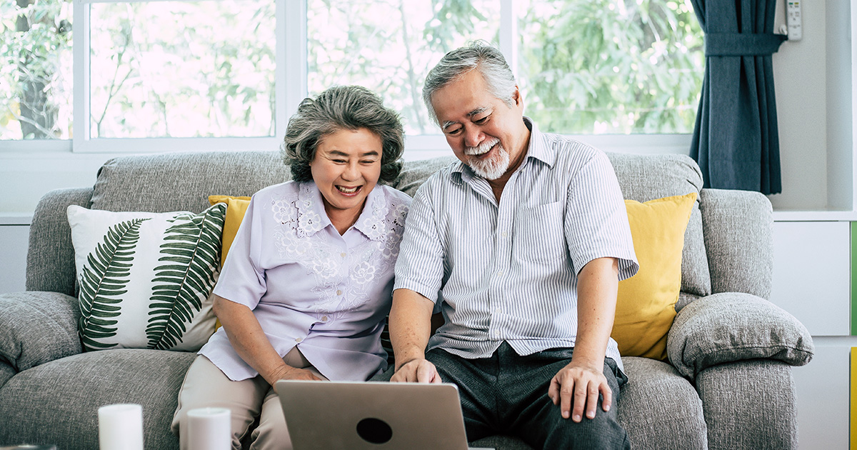 Older Asian couple talking on couch with laptop