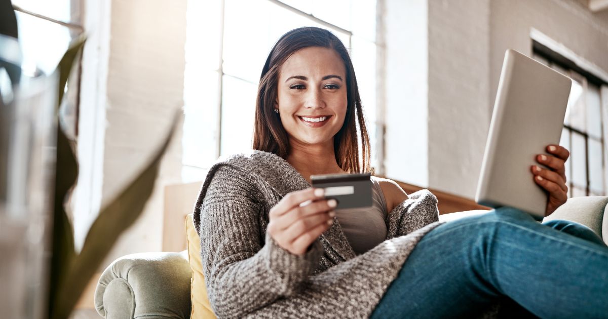 Woman holding a tablet and looking at her credit card.