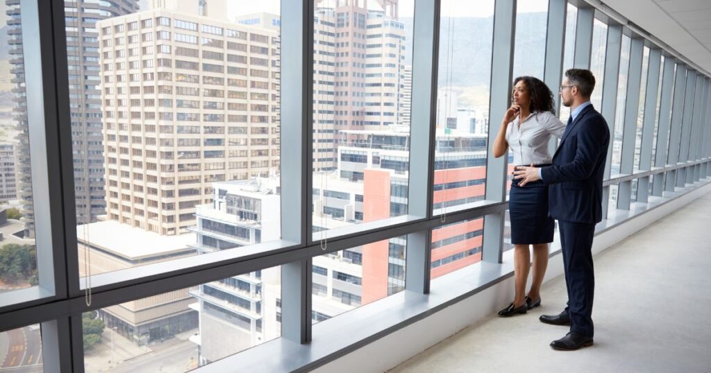 A man and a woman talking and looking out the window of a vacant office building