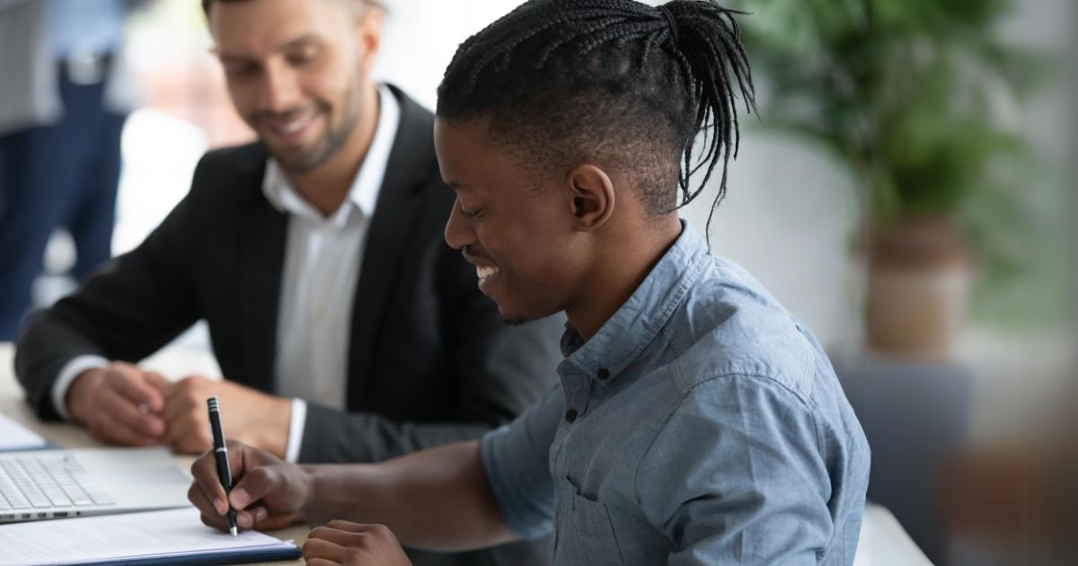 Young man at a desk signing papers with a financial advisor