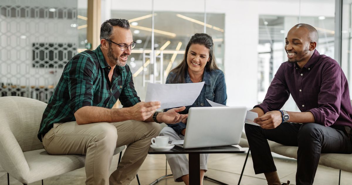 Two men and a woman in pleasant discussion over paperwork.