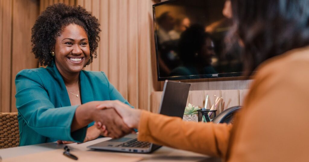 Two women smiling and shaking hands over a desk