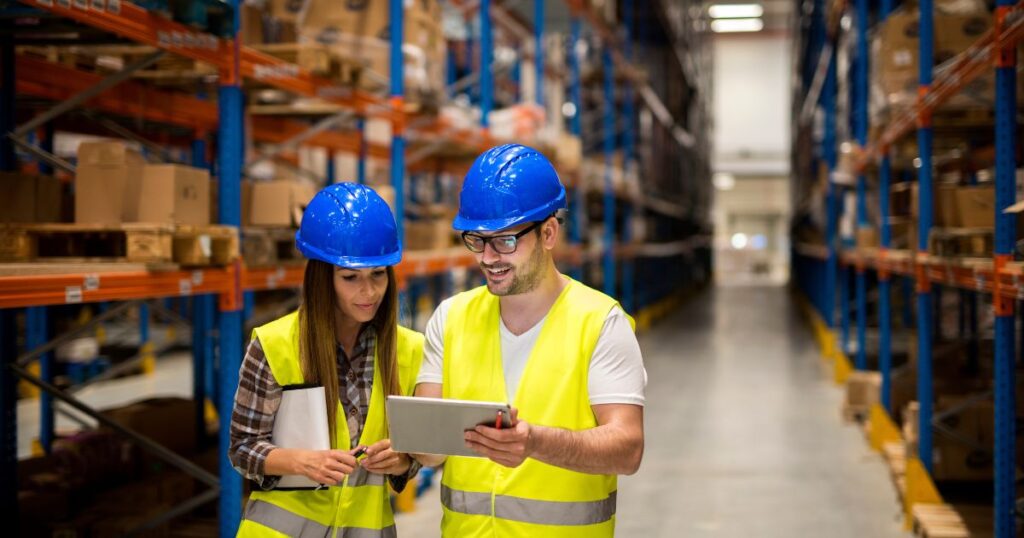 Woman and man wearing hardhats in warehouse discussing operations