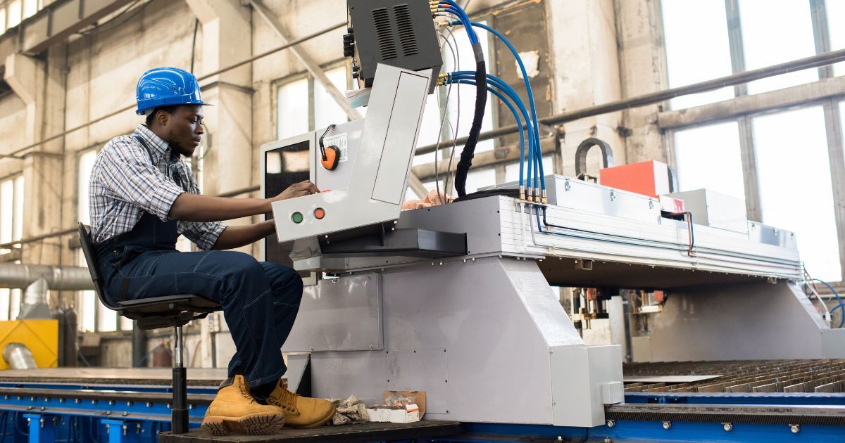 Man in hard hat sitting down while operating manufacturing machine