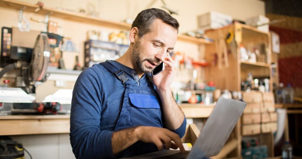 Man using his phone and laptop inside of a workshop