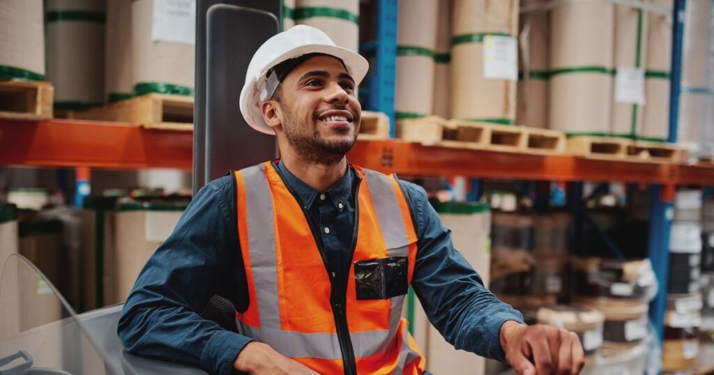 Smiling man wearing a hardhat while operating machine in warehouse