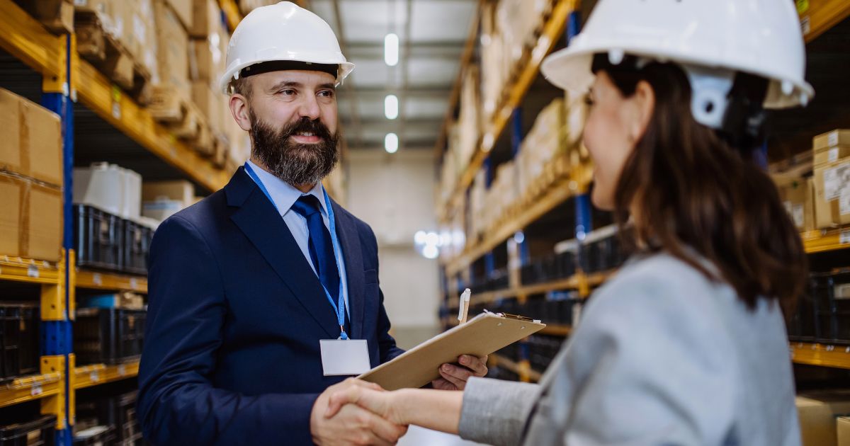 Woman and man in suits and hardhats shaking hands in a warehouse