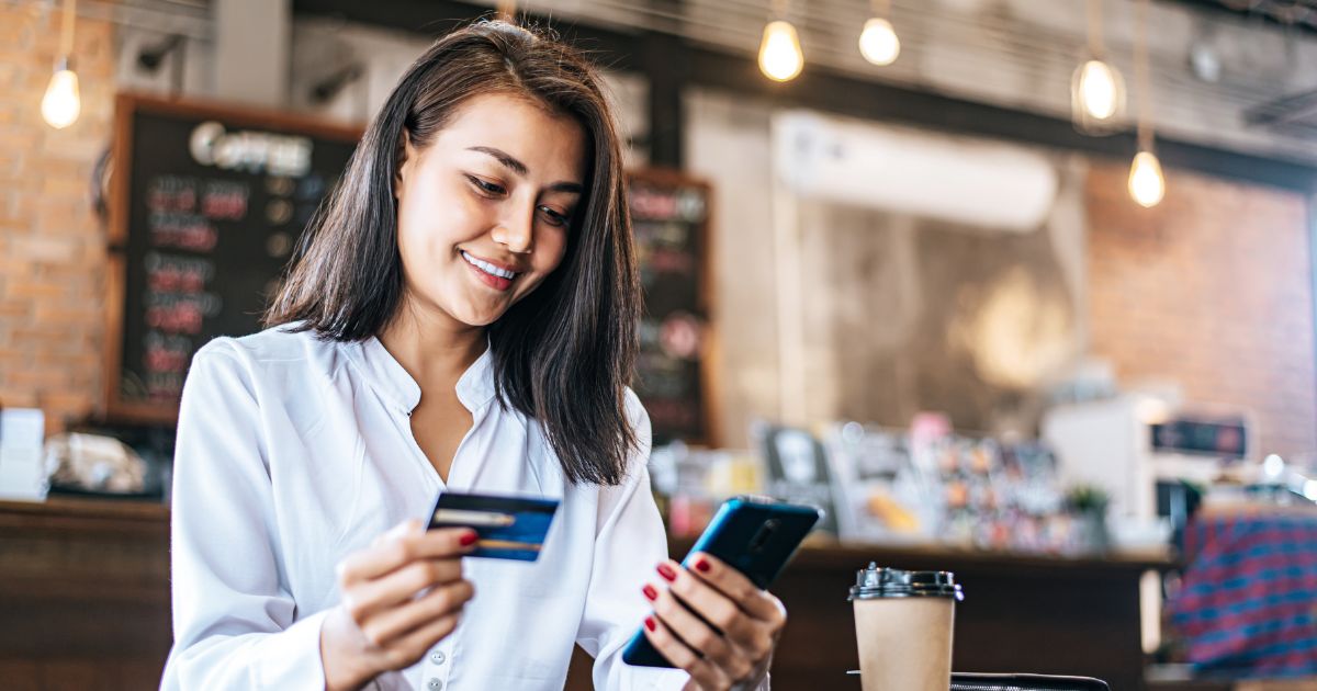 Woman on her phone paying with credit card in a coffee shop