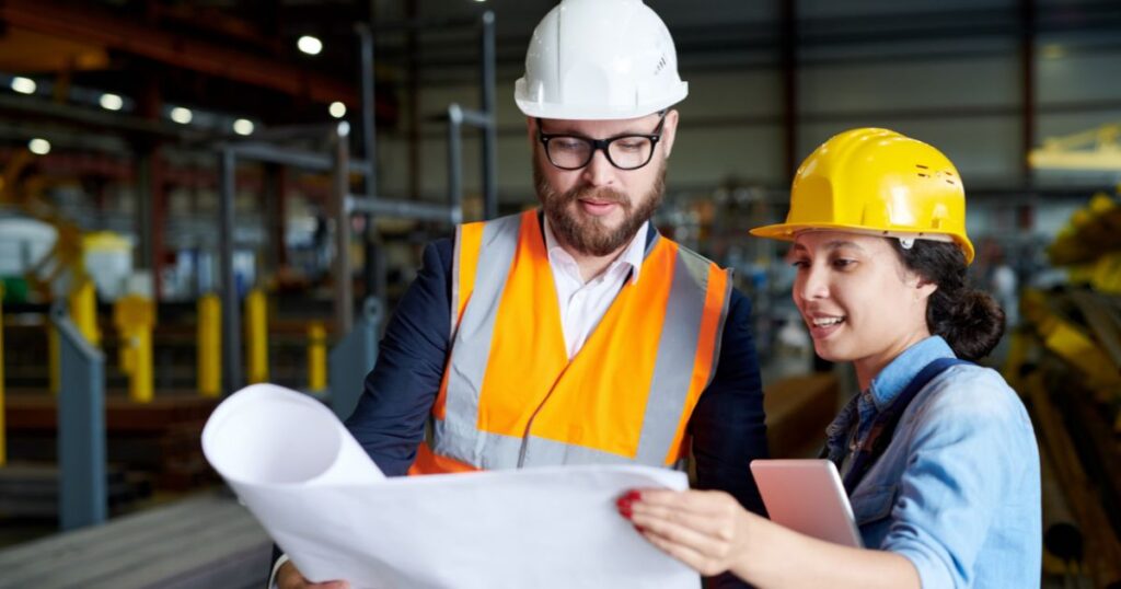 Woman and man in hardhats discussing blueprints in warehouse