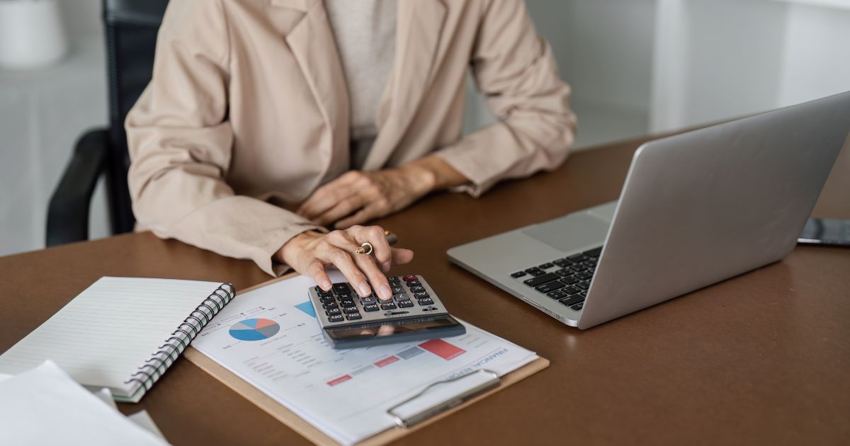 Woman sitting at desk with laptop and calculator.